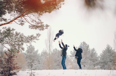 Aile kış parkında eğlenir. Mavi ceketli şık bir anne. Kışlık elbiseli küçük kız. Babası ve tatlı kızı.