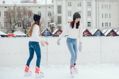 Kış şehrindeki kızlar. Beyaz kazaklı güzel bayanlar. Buz arenasında kadınlar