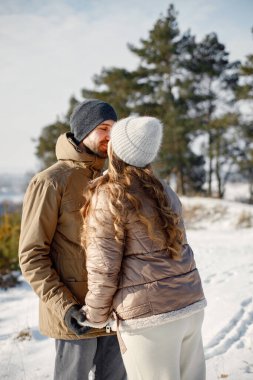 Kış yürüyüşünde eğlenen romantik çift portresi. Erkek ve kadın öpüşüyor. Aile ceketi ve örgü şapkalar giyiyor..