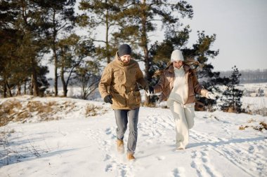 Kış yürüyüşünde eğlenen romantik çift portresi. Erkek ve kadın el ele tutuşuyor. Aile ceketi ve örgü şapkalar giyiyor..