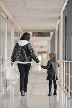 Anne ve kızı alışverişe çıkmış. Genç ve güzel müşteriler, cam duvarın önünde ellerinde poşetlerle bekliyorlar. Esmer kadın ve kızı siyah elbiseler giyiyordu..