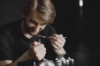 karanlık odada oturan ve çakmak eroin kaşıkla Isıtma keş adam.