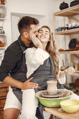 Ortak yaratıcı çalışma. Günlük giysiler ve önlükler içinde genç ve güzel bir çift. İnsanlar kilden bir stüdyoda çömlek çarkında kase yapıyorlar..