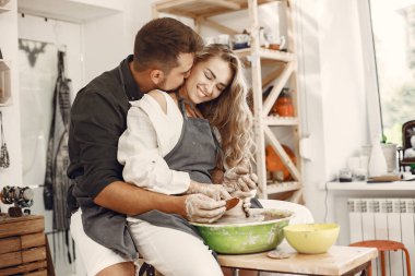 Ortak yaratıcı çalışma. Günlük giysiler ve önlükler içinde genç ve güzel bir çift. İnsanlar kilden bir stüdyoda çömlek çarkında kase yapıyorlar..