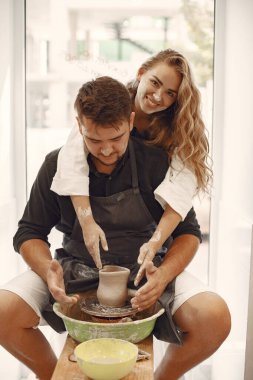 Ortak yaratıcı çalışma. Günlük giysiler ve önlükler içinde genç ve güzel bir çift. İnsanlar kilden bir stüdyoda çömlek çarkında kase yapıyorlar..