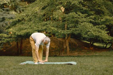 Beyaz tişörtlü son sınıf öğrencisi parkta duruyor ve antrenman yapıyor. Olumlu olgun kadınlarda fitness ya da yoga dersi vardır. Emeklilikte sağlık ve sağlıklı yaşam tarzı.