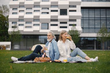 Yazın parkta çimlerin üzerinde oturan güzel beyaz yaşlı bir çift. Kadın ve erkek parkta battaniyeye oturmuş meyve suyu içiyor ve birkaç değerli anı paylaşıyorlar. Beyaz gömlekli kadın.