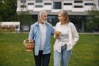 Yazın çimlerin üzerinde duran Kafkasyalı yaşlı çift. Saman sepeti tutan adam ve kadın çiçekleri. Beyaz tişörtlü kadın ve mavi erkek..