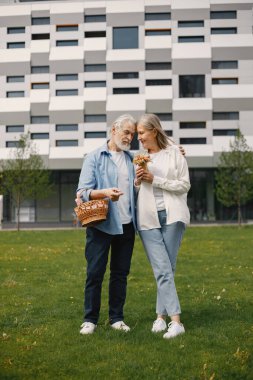 Yazın çimlerin üzerinde duran Kafkasyalı yaşlı çift. Saman sepeti tutan adam ve kadın çiçekleri. Beyaz tişörtlü kadın ve mavi erkek..