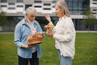 Yazın çimlerin üzerinde duran Kafkasyalı yaşlı çift. Saman sepeti tutan adam ve kadın çiçekleri. Beyaz tişörtlü kadın ve mavi erkek..