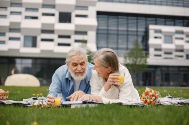 Yazın çimlerin üzerinde battaniyeye uzanmış beyaz yaşlı bir çift. Erkek ve kadın kitap okuyor ve meyve suyu içiyor. Beyaz tişörtlü kadın ve mavi erkek..