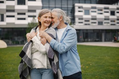 Yazın çimlerin üzerinde duran Kafkasyalı yaşlı çift. Erkek ve kadın sarılıyor. Beyaz gömlekli ve ekose battaniyeli bir kadın..