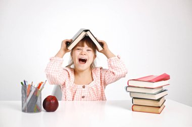 Down sendromlu güneşli bir kız masada oturuyor ve kafasının üstünde açık bir kitap tutuyor. Kız evde yalnız çalışıyor. Engelli çocuk konsepti eğitimi.
