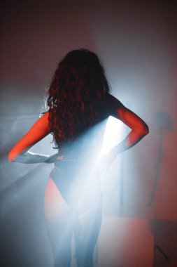 Genç kıvırcık esmer kız fotoğraf için poz veriyor. Kırmızı kadife giysili kız. Projektörler kızı aydınlatıyor..