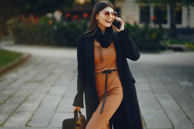 Styligh kadını güneşli bir günde şehirde yürürken cep telefonunu kullanır.