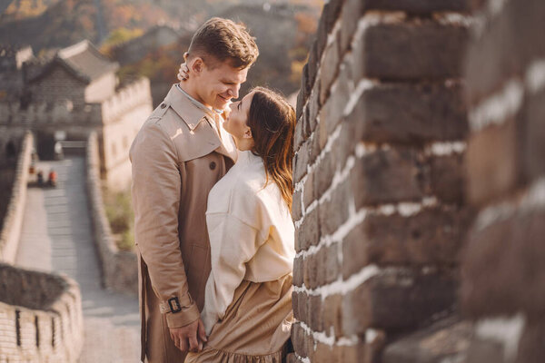 beautiful young couple hugging at the Great Wall of China. Newly married couple on their honemoon to Great Wall near Beijing China. Stylish couple exploring one of the wonders of the world.