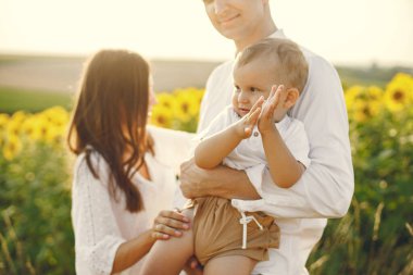 Güneşli bir günde, ayçiçeği tarlasında genç bir ailenin fotoğrafı. Esmer anne, baba ve küçük sarışın oğulları fotoğraf için poz veriyorlar. Erkek ve kadın oğullarına sarılıyor..