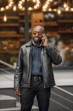 Şehirdeki bir caddede duran siyah adam. Güneş gözlüklü ve deri ceketli bir adam. Telefon eden bir iş adamı..