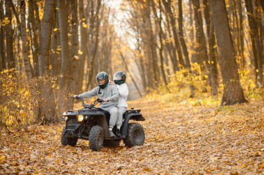 A young caucasian man and woman riding an ATV quad bike in autumn forest. Couple maneuvering off-road ATV. Couple wearing grey sportive costumes.