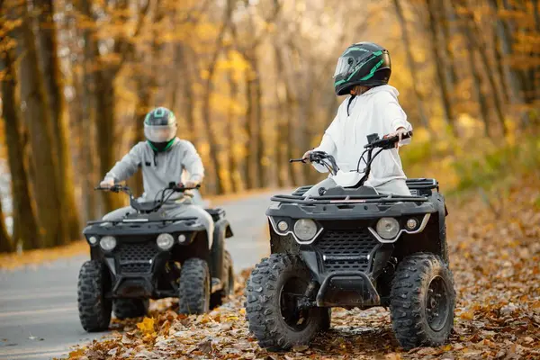 A young caucasian man and woman riding an ATV quad bikes in autumn forest. Two friends maneuvering off-road ATV. Couple wearing grey sportive costumes.