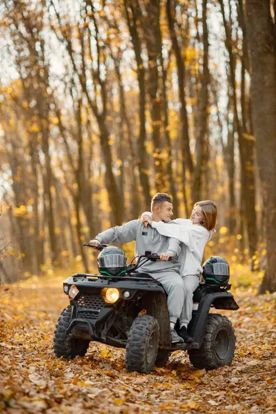 A young caucasian man and woman riding an ATV quad bike in autumn forest. Lovely couple hugging. Couple wearing grey sportive costumes.