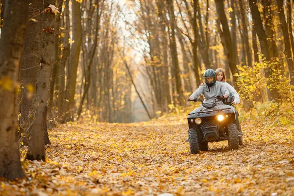 A young caucasian man and woman riding an ATV quad bike in autumn forest. Couple maneuvering off-road ATV. Couple wearing grey sportive costumes.