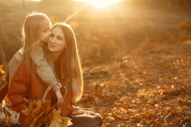 Kızı olan modaya uygun bir anne. Sonbahar parkında bir aile. Kahverengi ceketli küçük kız..