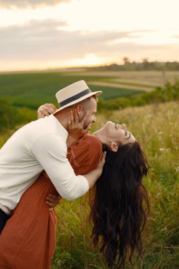 Couple in a field. Woman in a brown dress. Sunset background.