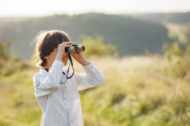 Tarlada dürbünü olan küçük bir kâşifin portresi. Yazın tarlada dürbünden bakan beyaz bir çocuk. Esmer çocuk çizgili gömlek giyiyor..