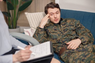 Asker terapi sırasında kanepede yatıyor. Askeri üniforma giyen adam. Psikiyatristle konuşan erkek savaşçı..