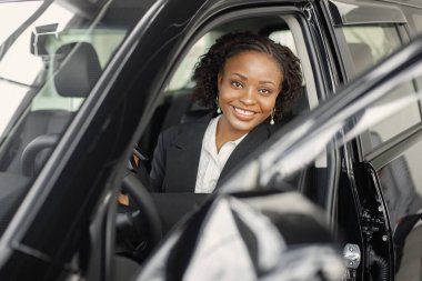 Young and cheerful woman enjoying new car while sitting inside. Black woman driving a car. Girl wearing black costume.