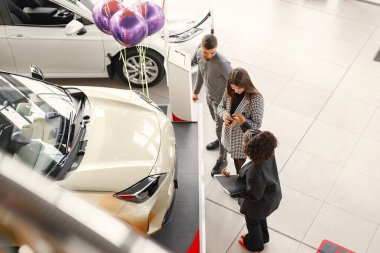 Professional car dealer standing at auto showroom. Man and woman want to buy a car. Photo from a second floor.