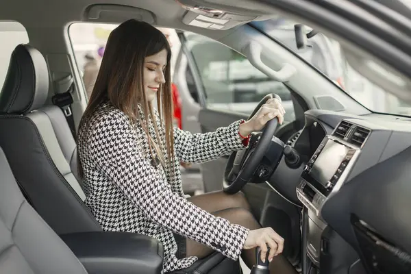 Genç ve neşeli bir kadın içeride otururken yeni arabasının keyfini çıkarıyor. Araba kullanan bir kadın. Gri ceketli kız..