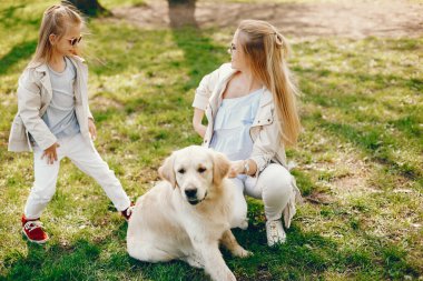 güneşli bir yaz parkında onu küçük sevimli kızı ile oynarken açık saçlı ve ceket ile güzel ve zarif genç anne ve köpek ile oynamak.