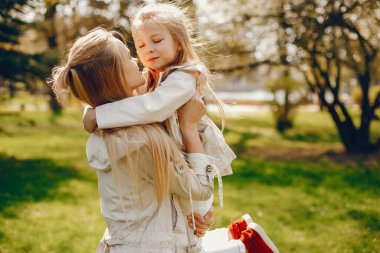 güneşli bir yaz parkında onu küçük sevimli kızı ile oynarken açık saçlı ve ceket ile güzel ve zarif genç anne