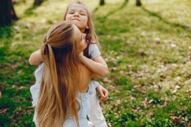 güneşli bir yaz parkında onu küçük sevimli kızı ile oynarken açık saçlı ve ceket ile güzel ve zarif genç anne