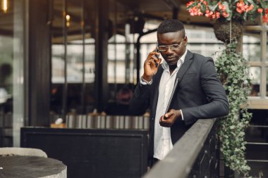 African man. Guy in a black suit. Male with a mobile phone. Businessman at the office.