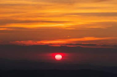 Kırmızı, büyük, yükselen güneş altın turuncu gökyüzünün ortasında batmak üzere..