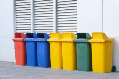 Bina duvarında farklı geri dönüşüm sembolleri olan sarı, yeşil, mavi ve kırmızı geri dönüşüm kutuları