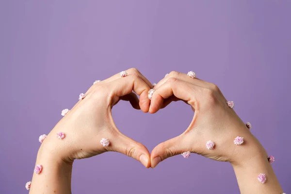 Heart hand gesture on purple. Small flowers on skin, spring vibe