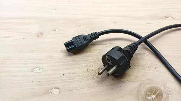 Jakarta, Indonesia - December 23, 2022: three hole laptop power adapter cable with wooden background