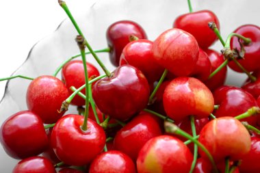 Beyaz arka planda kırmızı kirazlar. Yakın plan bir tabakta tatlı kirazlar. Yeşil kuyruklu bir sürü tatlı kiraz. Sulu kiraz meyveleri.