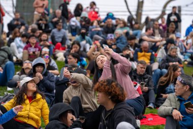 Toronto, Kanada - 8 Nisan 2024: İnsanlar Riverdale Park 'taki kısmi güneş tutulmasının başlangıcını özel tutulma gözlüklerini takarak izliyorlar. 