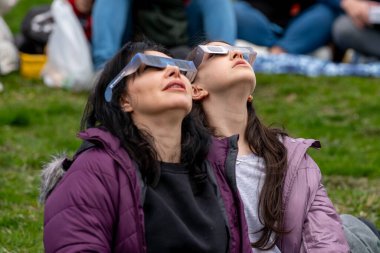 Toronto, Kanada - 8 Nisan 2024: Riverdale Park 'ta kısmi güneş tutulmasının başlangıcını izleyen kadın ve kız, özel güneş tutulması gözlüğü takıyorlar.. 