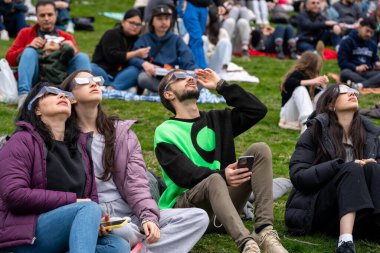 Toronto, Kanada - 8 Nisan 2024: İnsanlar Riverdale Park 'taki kısmi güneş tutulmasının başlangıcını özel tutulma gözlüklerini takarak izliyorlar. 