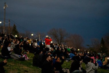 Toronto, Canada - April 8, 2024: People watch the beginning of the partial solar eclipse at Riverdale Park, wearing their special eclipse glasses.  clipart