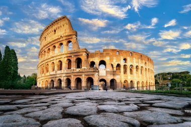 Roma, İtalya 'da gün batımında Kolezyum. Colosseum 'un ana cephesinin alçak açılı görüntüsü ve ön planda parlayan taş levhaların antik asfaltları..