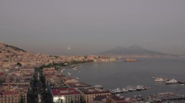 İtalya 'daki Napoli Körfezi manzarası, ön planda marina, arka planda deniz önü ve Vesuvius. Dolunay ufuktan yükseliyor..