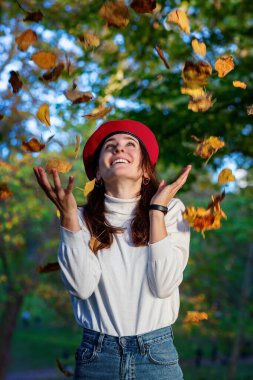 Kırmızı bereli kız ormandaki kuru sonbahar yapraklarını havaya fırlatıyor..