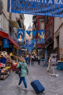 Napoli, İtalya - 21 Nisan 2023: San Gregorio Armeno 'nun tarihi merkezinde, şehrin futbol takımının sembolleriyle süslenmiş sokaklarda, bavulunu taşıyan bir turist.